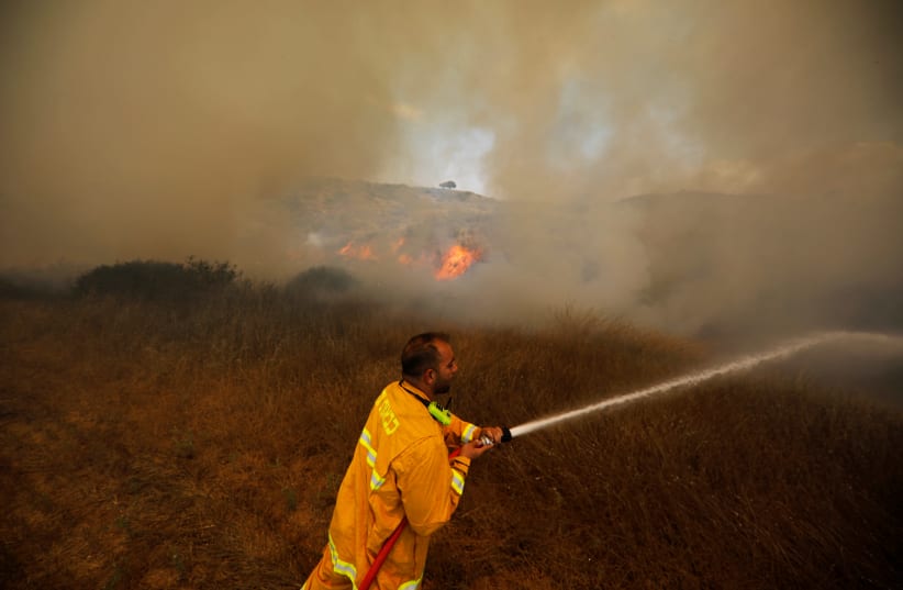A firefighter attempts to extinguish a fire burning scrubland in an area where Palestinians have been causing blazes by flying kites and balloons loaded with flammable materials, on the Israeli side of the border between Israel and the Gaza Strip, near kibbutz Nir Am, June 5, 2018 (photo credit: AMIR COHEN/REUTERS)