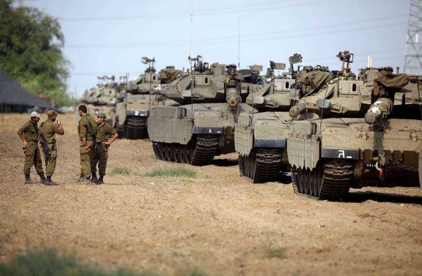 Israeli soldiers speak next to tanks as military armoured vehicles gather in an open area near Israel's border with the Gaza Strip October 18, 2018.  (photo credit: REUTERS/AMIR COHEN)