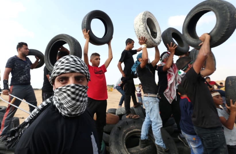 A masked Palestinian demonstrator gestures as others hold tires during a protest at the Israel-Gaza border fence in the southern Gaza Strip October 19, 2018. (photo credit: IBRAHEEM ABU MUSTAFA / REUTERS)