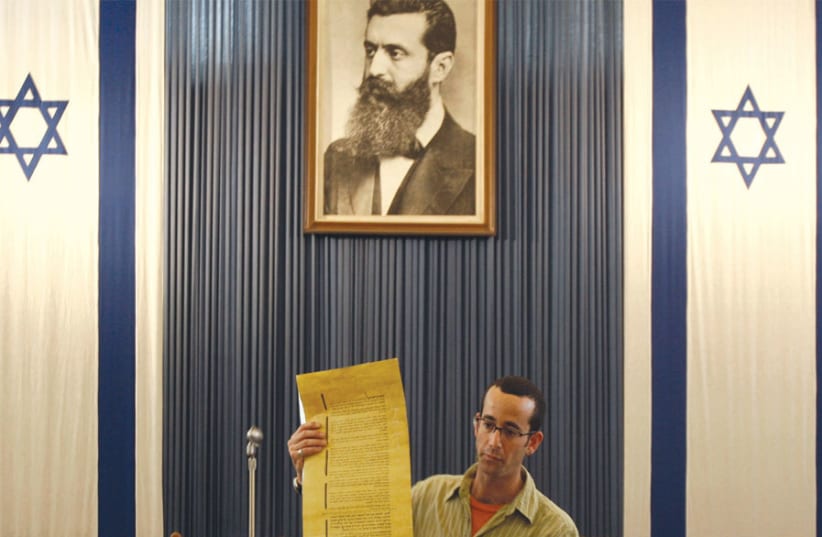 A guide stands under a portrait depicting Theodor Herzl, the father of modern Zionism, as he holds a copy of Israel’s Declaration of Independence in the building where it was first read by David Ben-Gurion in Tel Aviv (photo credit: LIORA MIZRAHI / REUTERS)