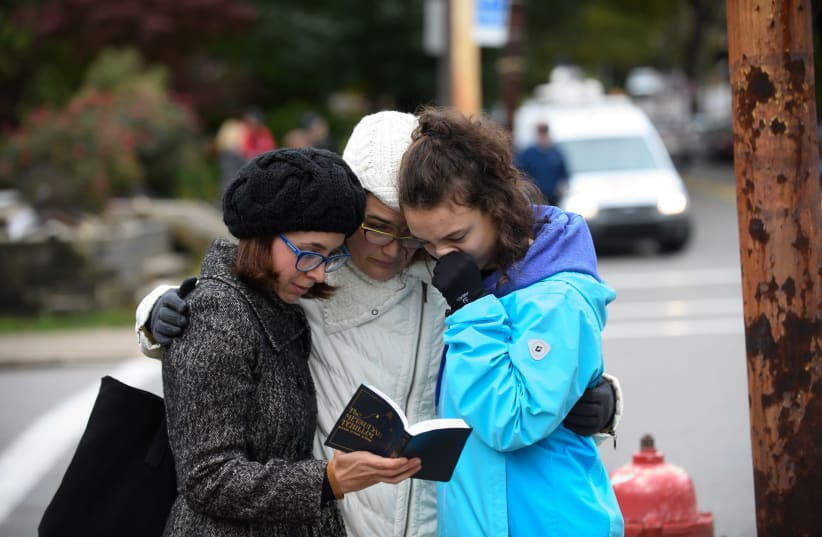 Tammy Hepps, Kate Rothstein and her daughter, Simone Rothstein, 16, pray from a prayerbook a block away from the site of a mass shooting at the Tree of Life Synagogue in the Squirrel Hill neighborhood on October 27, 2018 in Pittsburgh, Pennsylvania (photo credit: JEFF SWENSEN / GETTY IMAGES NORTH AMERICA / AFP)