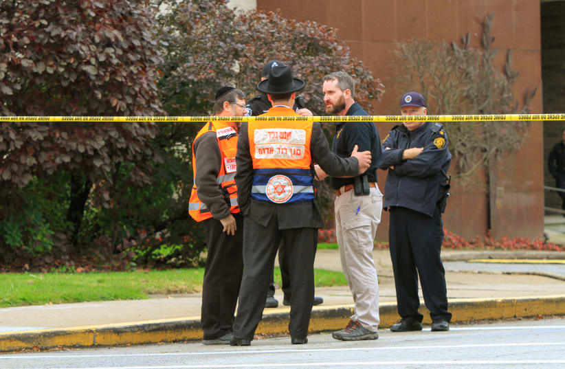 Police officers guarding the Tree of Life synagogue following shooting at the synagogue, speak with men in orange vest from a Jewish burial society in Pittsburgh, Pennsylvania, US, October 27, 2018 (photo credit: REUTERS/JOHN ALTDORFER)