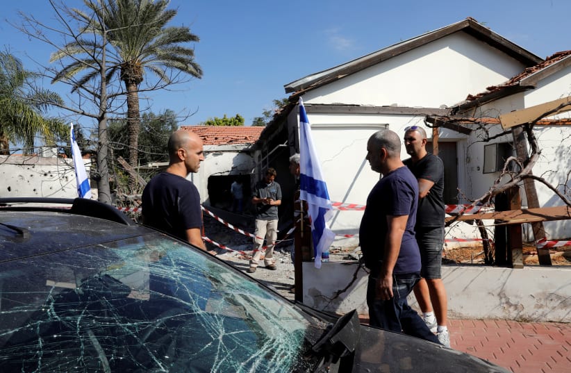 People stand next to a car and house damaged by a rocket fired from the Gaza Strip, in the Israeli city of Ashkelon November 13, 2018 (photo credit: RONEN ZVULUN / REUTERS)