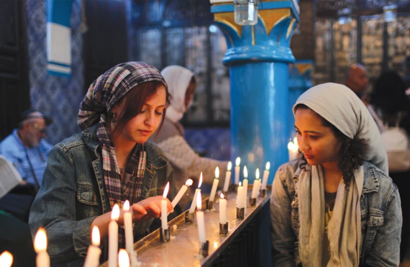 A Tunisian Muslim woman buys food from a Jewish restaurant in DjerbaCyrine Ben Said (left) and Amnia Ben Khalif, Muslim Tunisians, light candles during a religious ceremony at El Ghriba, the second oldest Jewish synagogue in Africa (photo credit: AHMED JADALLAH / REUTERS)