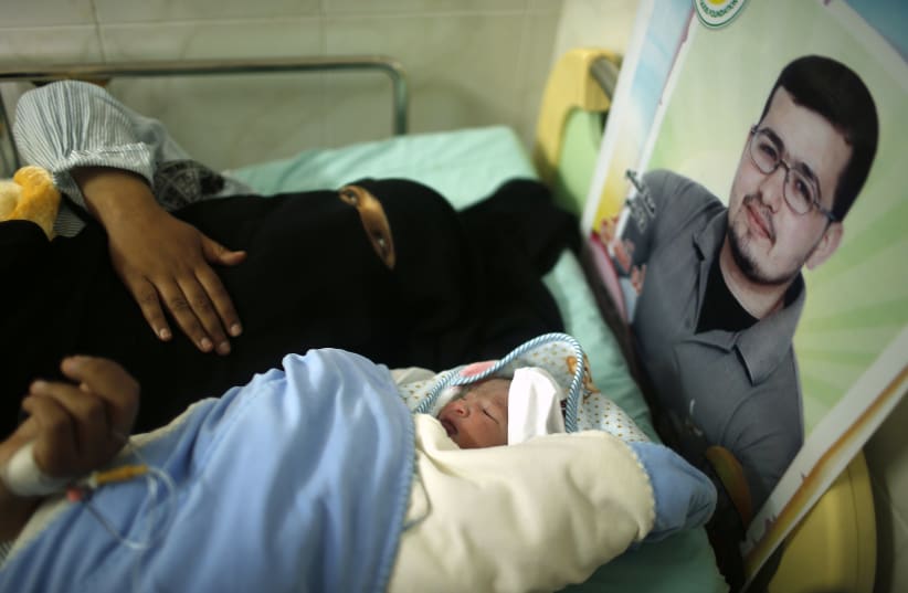 Hana, the wife of Palestinian prisoner Tamer al-Za'anin (pictured in poster), lies on a bed next to her baby boy al-Hassan, who was conceived with al-Za'anin's sperm smuggled out of an Israeli prison, at a hospital in Gaza City January 10, 2014 (photo credit: REUTERS/SUHAIB SALEM)
