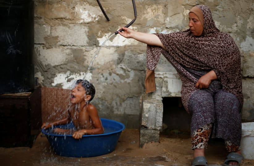 A Palestinian woman bathes her son with water from a tank, filled by a charity, inside their dwelling in Khan Younis, in the southern Gaza Strip (photo credit: MOHAMMED SALEM/REUTERS)
