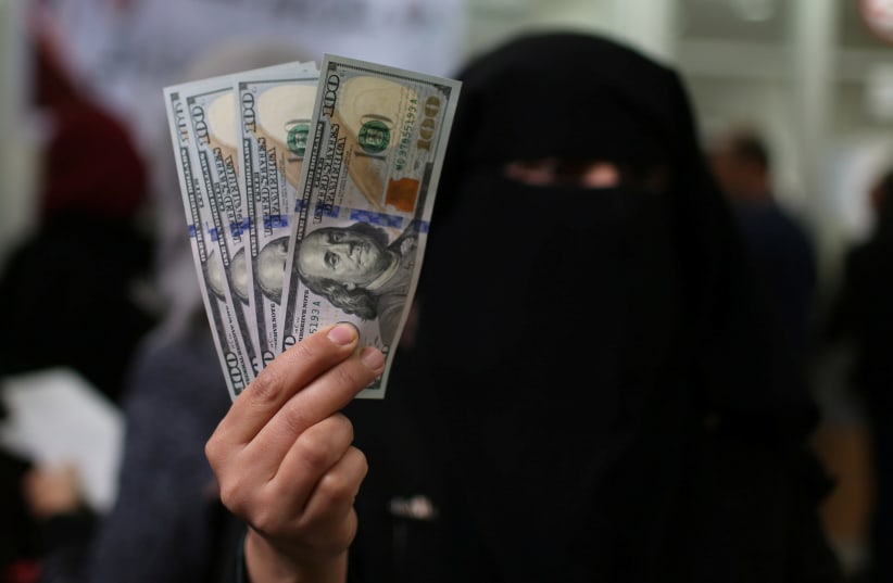A Palestinian Hamas-hired civil servant displays U.S. Dollar banknotes after receiving her salary paid by Qatar, in Khan Younis in the southern Gaza Strip December 7, 2018 (photo credit: IBRAHEEM ABU MUSTAFA / REUTERS)