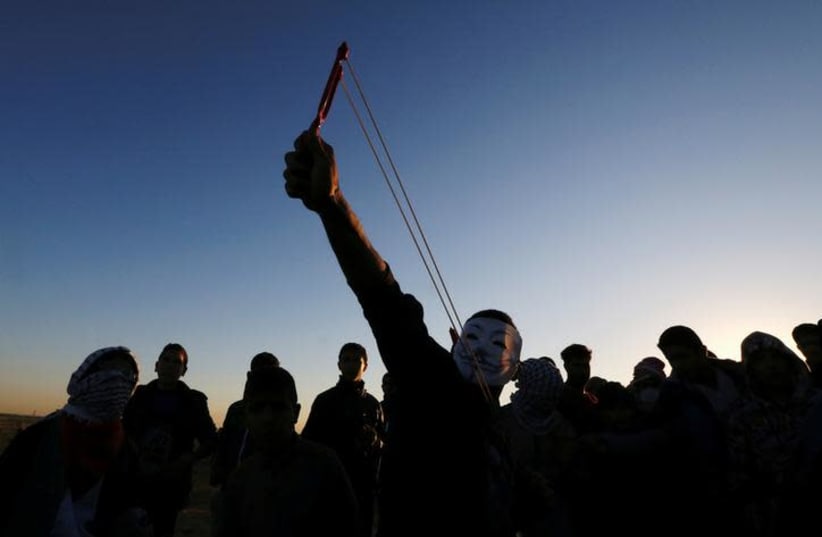 A Palestinian demonstrator uses a slingshot to hurl stones at Israeli troops during a protest at the Israel-Gaza border fence, in the southern Gaza Strip December 14, 2018. (photo credit: IBRAHEEM ABU MUSTAFA / REUTERS)