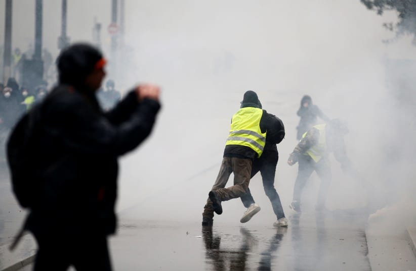 A man wearing a yellow vest tackles a protester as tear gas floats in the air during clashes with police at a demonstration by the "yellow vests" movement in Nantes, France, December 15, 2018 (photo credit: STEPHANE MAHE / REUTERS)