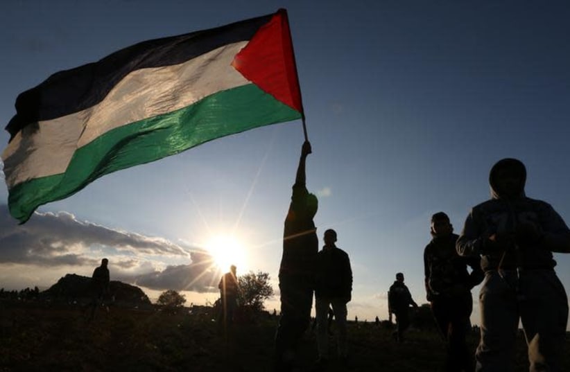 A demonstrator holds a Palestinian flag during a protest near the Israel-Gaza border fence, in the southern Gaza Strip December 21, 2018. (photo credit: REUTERS/IBRAHEEM ABU MUSTAFA)