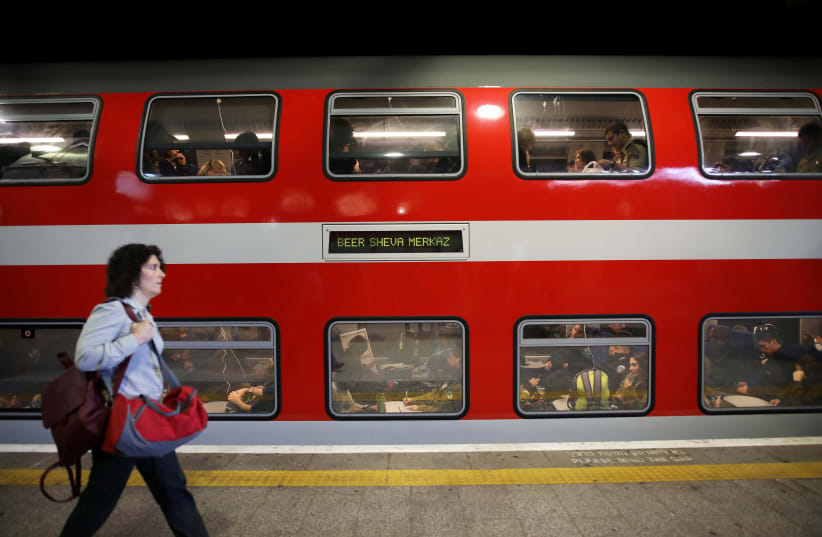A woman walks on a platform in front of a train as passengers are seen through the carriage windows at Tel Aviv's HaShalom train station, Israel November 25, 2018. Picture taken November 25, 2018 (photo credit: REUTERS/CORINNA KERN)