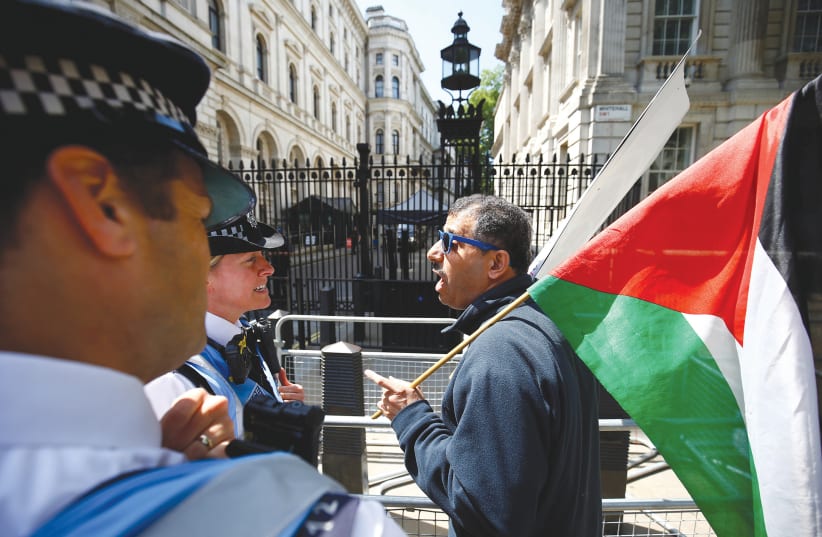 POLICE OFFICERS speak to a demonstrator holding a Palestinian flag in London ahead of Prime Minister Benjamin Netanyahu’s visit in June.  (photo credit: REUTERS)