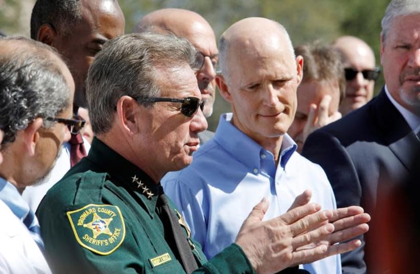 Broward County Sheriff Scott Israel speaks to the media while Florida Governor Rick Scott listens outside Marjory Stoneman Douglas High School one day after a shooting at the school left 17 dead, in Parkland, Florida, U.S. (photo credit: JONATHAN DRAKE / REUTERS)