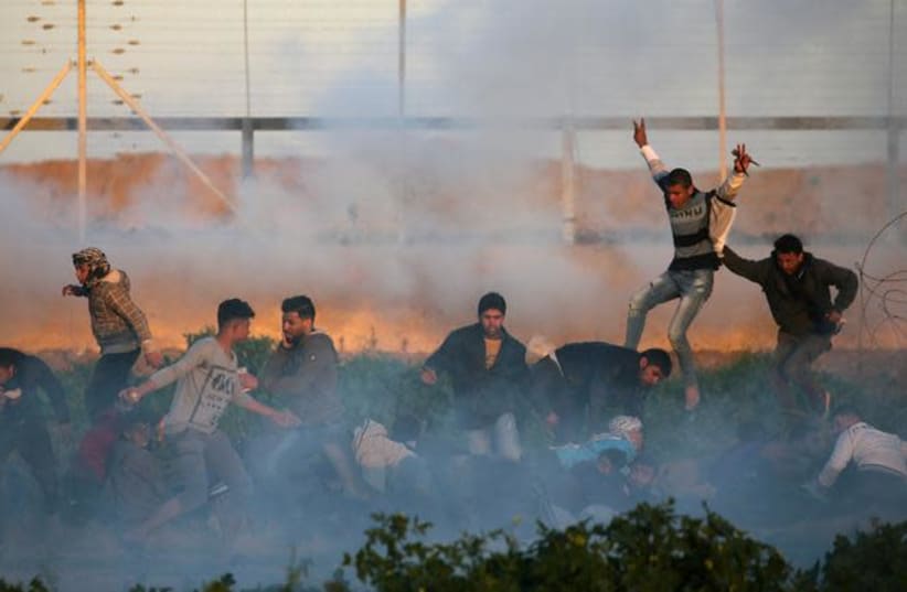 Palestinians run for cover from tear gas fired by Israeli forces during a protest at the Israel-Gaza border fence, in the southern Gaza Strip January 11, 2019 (photo credit: REUTERS/IBRAHEEM ABU MUSTAFA)
