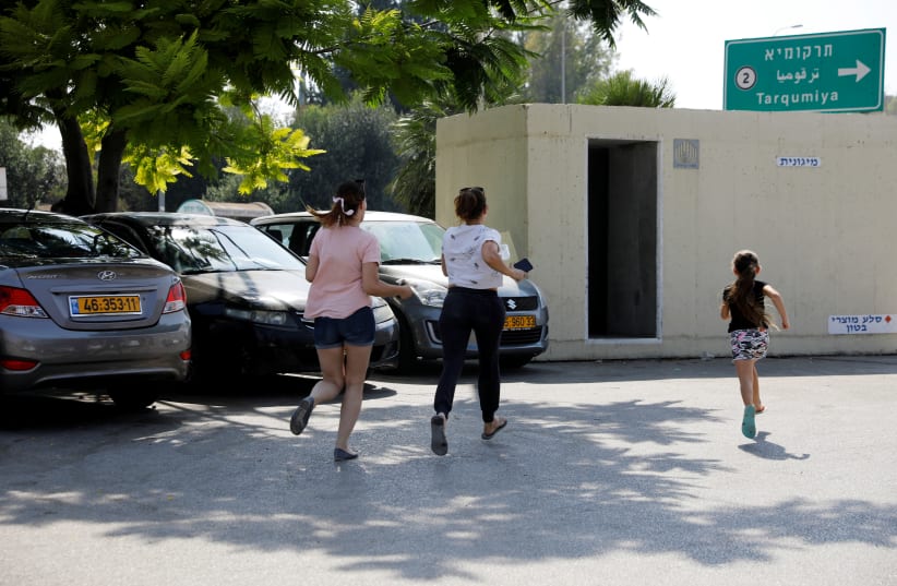 Israelis run for shelter as a siren sounds during a rocket attack near Yad Mordechai at the Israeli side of the Israel Gaza border July 14, 2018  (photo credit: AMIR COHEN/REUTERS)