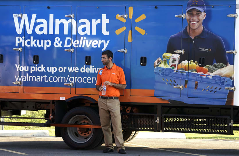 A Wal-Mart Pickup-Grocery employee waits next to a truck at a test store in Bentonville, Arkansas June 4, 2015. Customers using the store place their orders online and then pick up their merchandise in a drive-through. Wal-Mart will hold its annual meeting June 5, 2015.  (photo credit: RICK WILKING / REUTERS)
