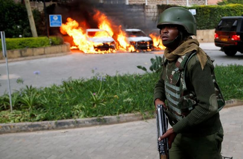 A policeman runs past burning cars at the scene where explosions and gunshots were heard at the Dusit hotel compound, in Nairobi, Kenya (photo credit: REUTERS/BAZ RATNER)