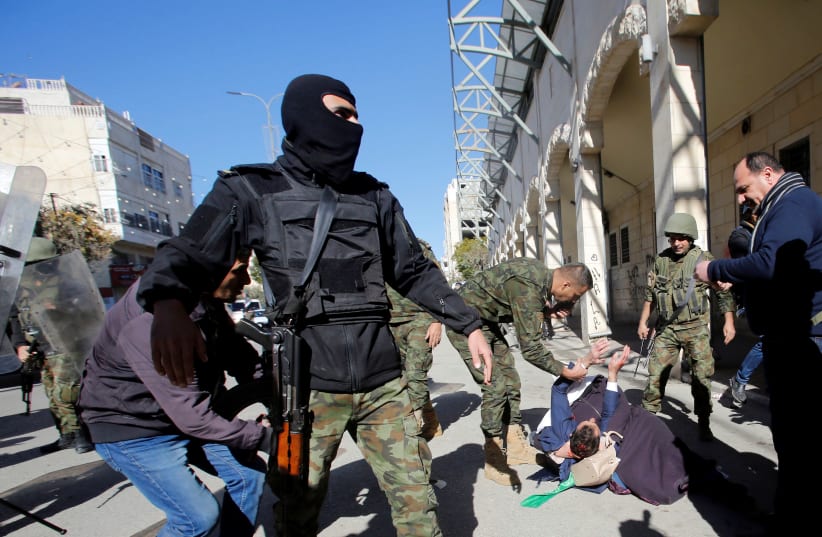A woman and a wounded protester fall on the ground as members of Palestinian security forces disperse a Hamas demonstration in the Palestinian Authority controlled side of Hebron, December 14, 2018 (photo credit: MUSSA QAWASMA / REUTERS)