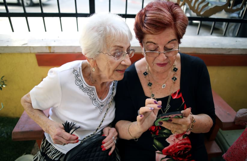 Holocaust survivors look at the mobile phone after they arrived to take part in the annual Holocaust survivors' beauty pageant in Haifa, Israel October 14, 2018 (photo credit: CORINNA KERN/REUTERS)