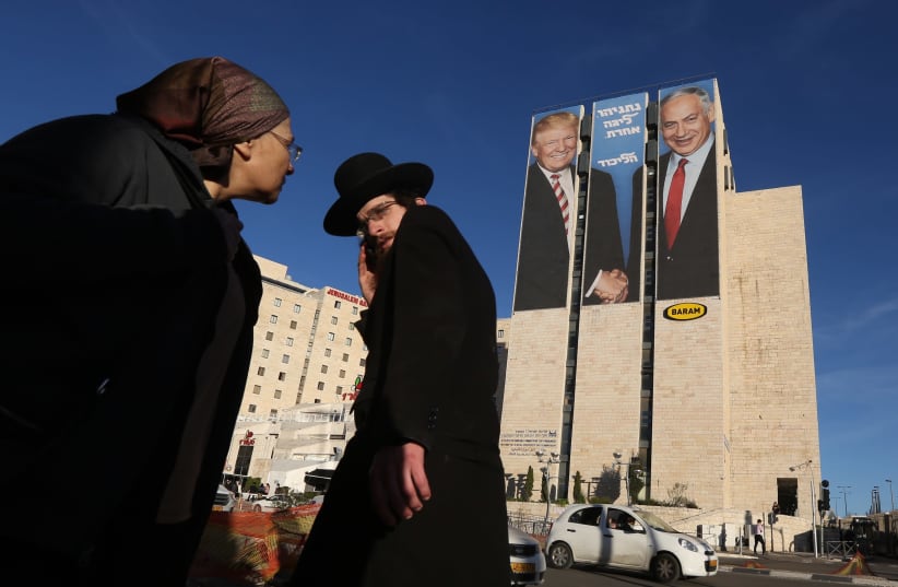 Residents of Jerusalem watch a billboard ad in which Prime Minister Benjamin Netanyahu is seen shaking hands with U.S. President Donald Trump, caption says: Netanyahu is in a whole other league   (photo credit: MARC ISRAEL SELLEM)