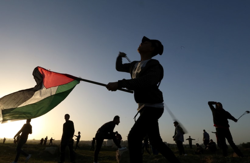 A demonstrator holding a Palestinian flag uses a sling to hurl stones at Israeli troops during a protest at the Israel-Gaza border fence, in the central Gaza Strip January 25, 2019 (photo credit: IBRAHEEM ABU MUSTAFA / REUTERS)