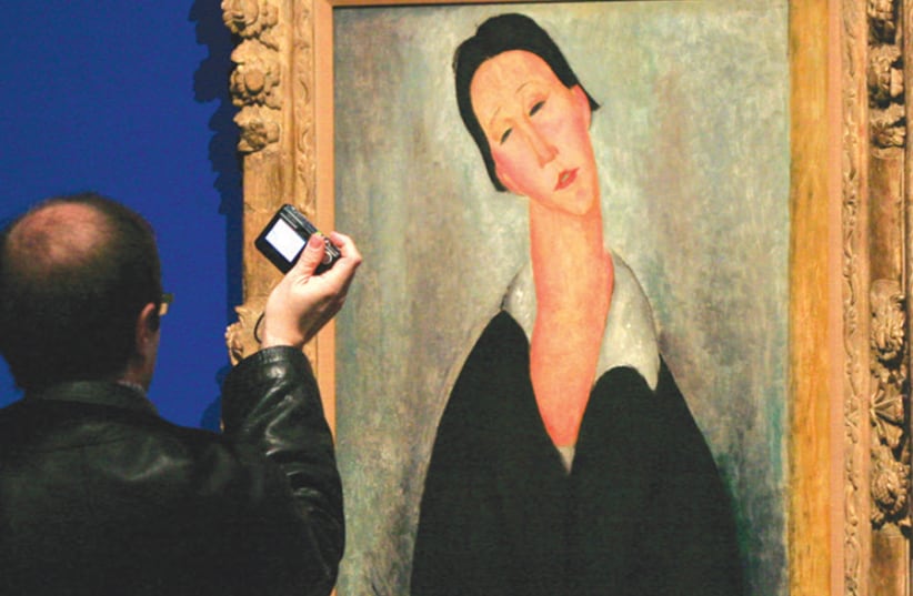A man photographs a painting entitled ‘Portrait de femme polonaise’ (Portrait of a Polish woman) painted in 1919 by Italian Jewish artist Amedeo Modigliani, at the Thyssen-Bornemisza Museum in Madrid (photo credit: PAUL HANNA/REUTERS)