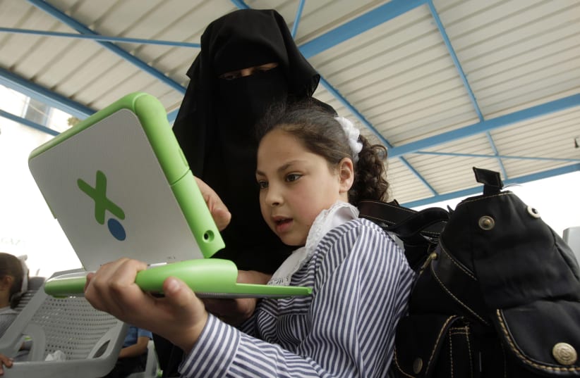 A teacher shows a Palestinian schoolgirl how to use a new laptop at a United Nations school in Gaza, April 29, 2010. (photo credit: IBRAHEEM ABU MUSTAFA / REUTERS)