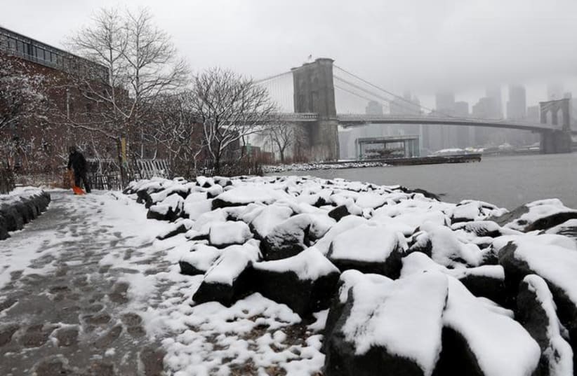 A woman shovels snow from a walkway at Brooklyn Bridge Park in New York, U.S., April 2, 2018 (photo credit: REUTERS/SHANNON STAPLETON)