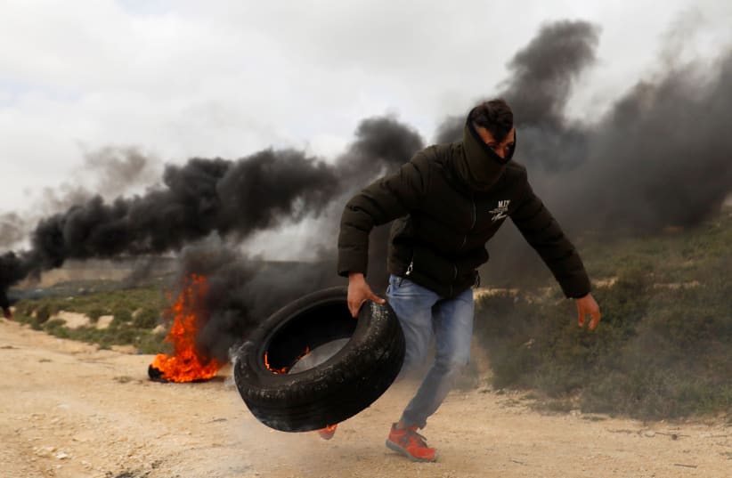 A Palestinian moves a tire during clashes with Israeli troops at a protest against Jewish settlements in the village of Oref, in the West Bank (photo credit: MOHAMAD TOROKMAN/REUTERS)