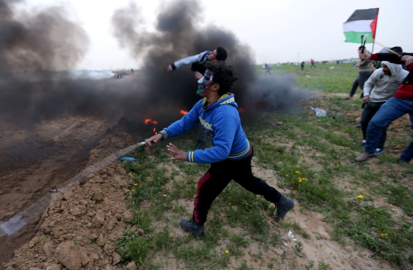 Palestinians hurl stones at Israeli troops during a protest at the Israel-Gaza border fence, in the southern Gaza Strip February 15, 2019. (photo credit: IBRAHEEM ABU MUSTAFA / REUTERS)