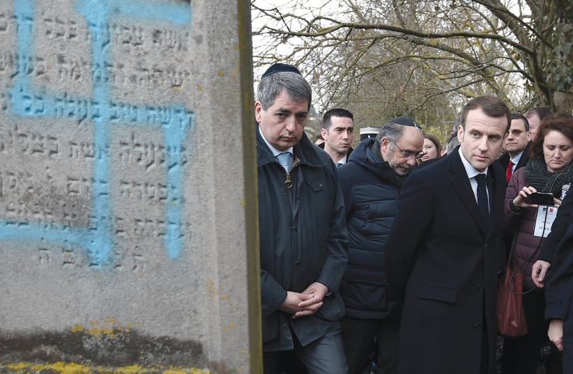 Emmanuel Macron looks at a grave defaced with a swastika during a visit to the Jewish cemetery in Quatzenheim on February 19. (photo credit: FREDERICK FLORIN/POOL/VIA REUTERS)