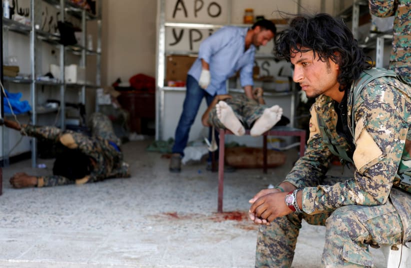 A Syrian Democratic Forces (SDF) fighter sits as medics treat his comrades injured by sniper fired by Islamic State militants in a field hospital in Raqqa, Syria, June 28, 2017. (photo credit: GORAN TOMASEVIC/REUTERS)