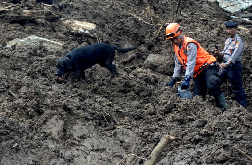 Indonesian police officers walk with dog as they search for victims following landslides in Gowa, South Sulawesi, Indonesia, January 26, 2019 in this photo taken by Antara Foto. Picture taken January 26, 2019 (photo credit: ANTARA PHOTO AGENCY VIA REUTERS)