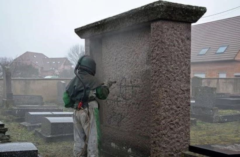 A worker removes antisemitic graffiti at a Jewish cemetery in France, March, 2019 (photo credit: FRANCE 3 ALSACE AND THE LOWER RHINE CONSISTORY)