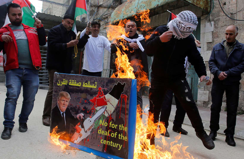 Protesters burn a poster of US President Donald Trump with the words "No for the deal of the century" in the Palestinian Authority controlled side of Hebron, February 22, 2019 (photo credit: MUSSA QAWASMA / REUTERS)