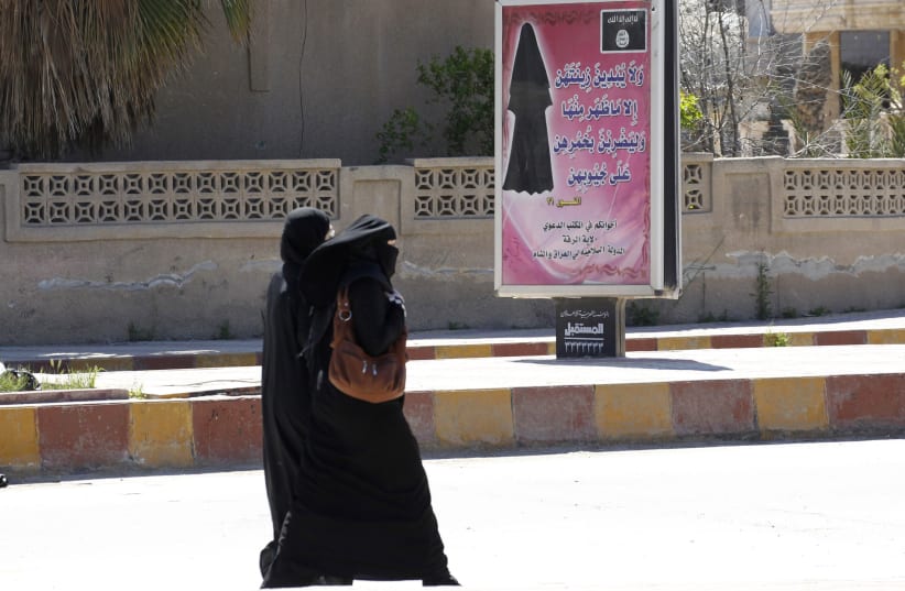 Veiled women walk past a billboard urging women to wear a hijab in Raqqa(REUTERS/Stringer) (photo credit: REUTERS/STRINGER)
