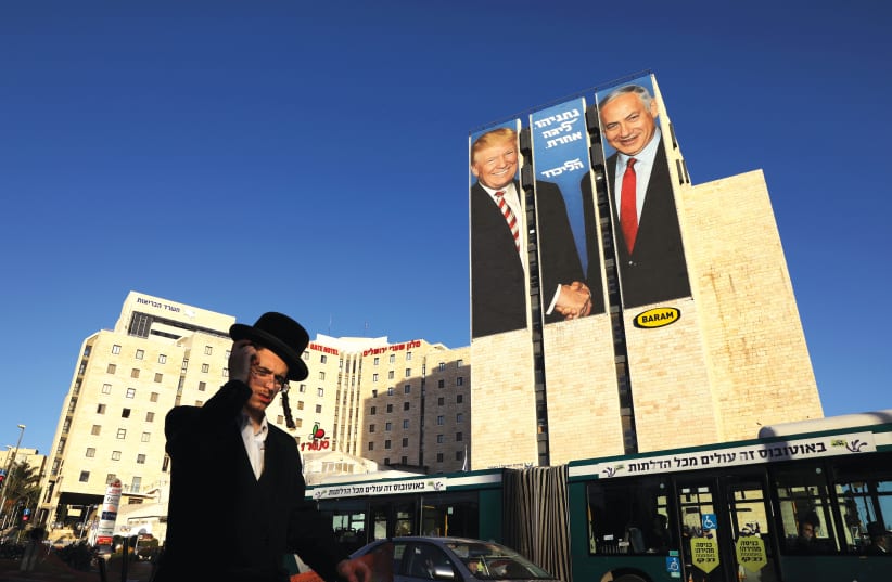 A MAN walks past a Likud election campaign billboard, depicting US President Donald Trump with Prime Minister Benjamin Netanyahu and the words, ‘Netanyahu. A different league’ (photo credit: AMMAR AWAD / REUTERS)