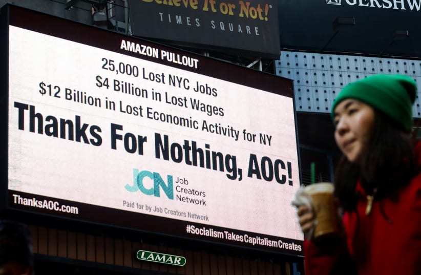 A woman passes by an electronic billboard in Times Square displaying, "Thanks For Nothing, AOC!", referencing U.S. Rep. Alexandria Ocasio-Cortez (D-NY) and the pullout of Amazon's HQ 2 in New York City, U.S., February 21, 2019 (photo credit: BRENDAN MCDERMID/REUTERS)