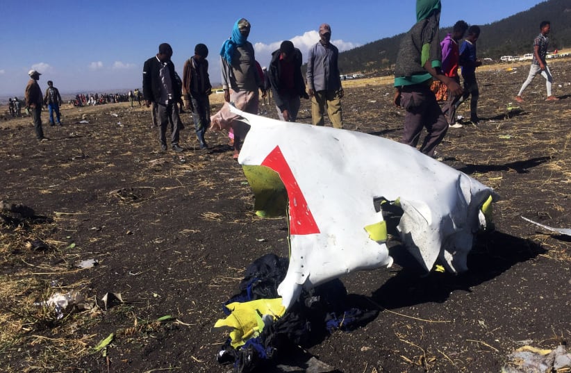 People walk past a part of the wreckage at the scene of the Ethiopian Airlines Flight ET 302 plane crash, near the town of Bishoftu, southeast of Addis Ababa, Ethiopia March 10, 2019 (photo credit: TIKSA NEGERI / REUTERS)