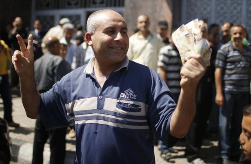 A Palestinian employee paid by the Palestinian Authority gestures as he holds money after withdrawing cash from an ATM machine outside a bank, in Gaza City (photo credit: REUTERS/MOHAMMED SALEM)