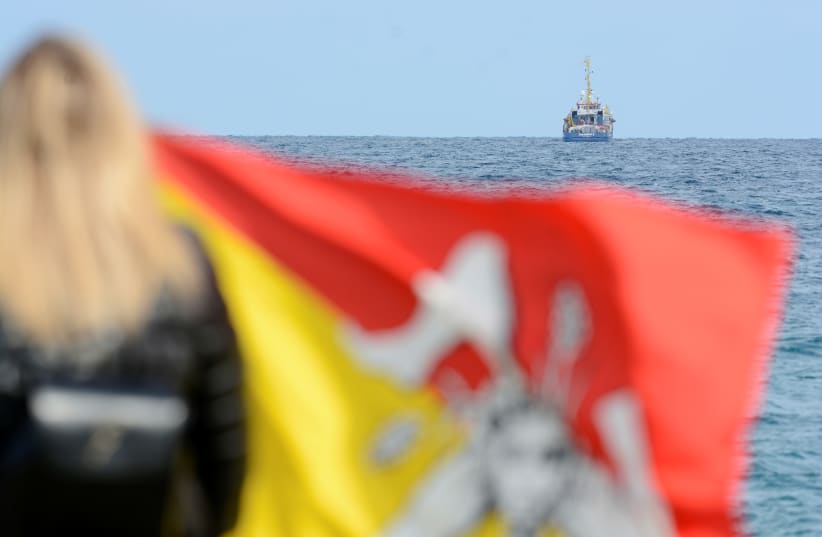 A woman holds a Sicilian flag as she looks at the migrant search and rescue ship Sea-Watch 3, operated by German NGO Sea-Watch off the coast of Siracusa, Italy, January 26, 2019.  (photo credit: GUGLIELMO MANGIAPANE / REUTERS)