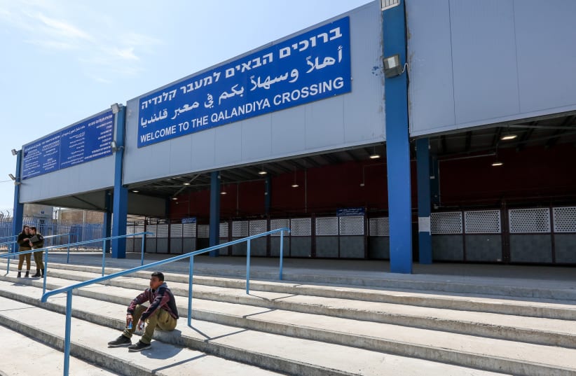 A young Palestinian sits and two IDF soldiers stand at the entrance of the Qalandiya crossing, 2019. (photo credit: MARC ISRAEL SELLEM)