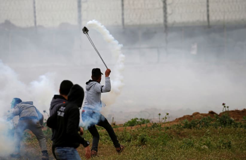 A Palestinian demonstrator uses a sling to hurl back a tear gas canister fired by Israeli forces during a protest marking Land Day and the first anniversary of a surge of border protests, at the Israel-Gaza border fence east of Gaza City March 30, 2019 (photo credit: MOHAMMED SALEM/REUTERS)