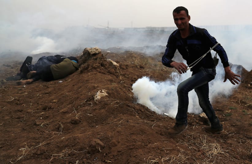 A Palestinian demonstrator reacts as others take cover from Israeli gunfire and tear gas during a protest marking Land Day and the first anniversary of a surge of border protests, at the Israel-Gaza border fence east of Gaza City March 30, 2019. (photo credit: MOHAMMED SALEM/ REUTERS)