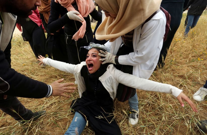 A Palestinian woman reacts after inhaling tear gas fired by Israeli forces during a protest marking Land Day and the first anniversary of a surge of border protests, at the Israel-Gaza border fence, in the southern Gaza Strip March 30, 2019.  (photo credit: ASHRAF ABU AMRAH / REUTERS)