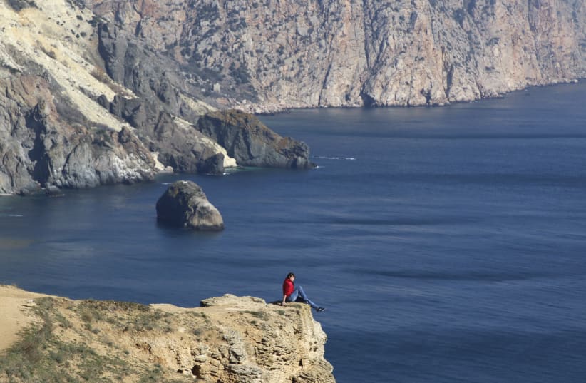 A woman sits on the edge of a cliff as she visits Cape Fiolent in the Black Sea port of Sevastopol, Crimea. (photo credit: REUTERS)