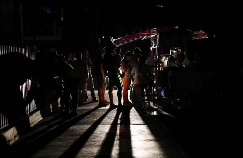 Locals gather at a street food cart during a blackout in Caracas (photo credit: IVAN ALVARADO/REUTERS)