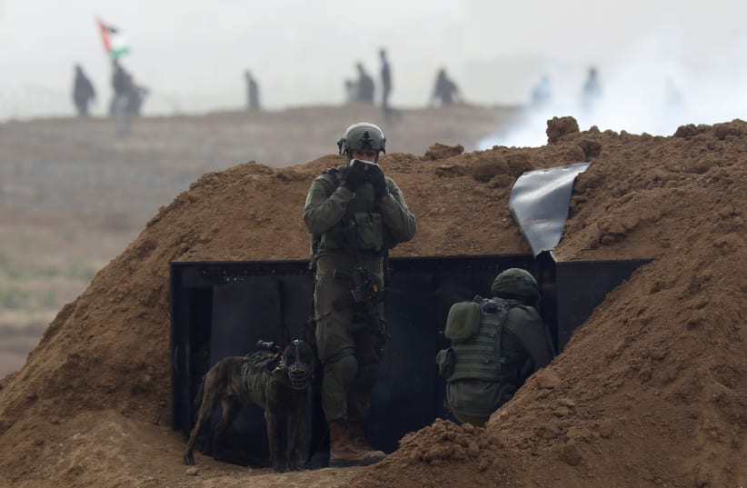 Israeli soldiers wait in position near the border fence between Israel and the Gaza Strip, during a protest on the Gaza side, as seen from the Israeli side March 30, 2019 (photo credit: REUTERS/AMIR COHEN)
