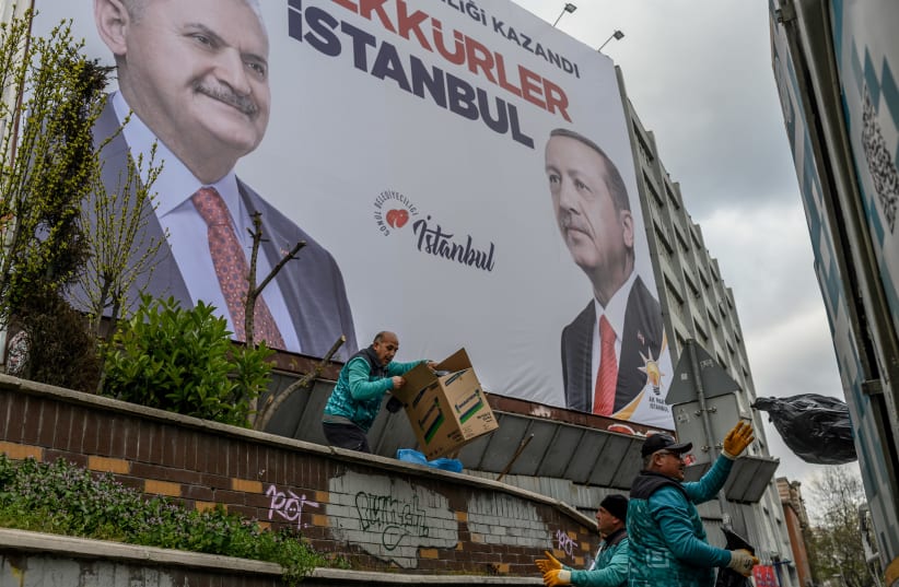 Workers pick up the garbage next to a billboard reading "Thank You Istanbul" and portraying AKP ruling party mayor candidate Binali Yildirim and President Recep Tayyip Erdogan, in Istanbul, on April 2, 2019 (photo credit: BULENT KILIC / AFP)
