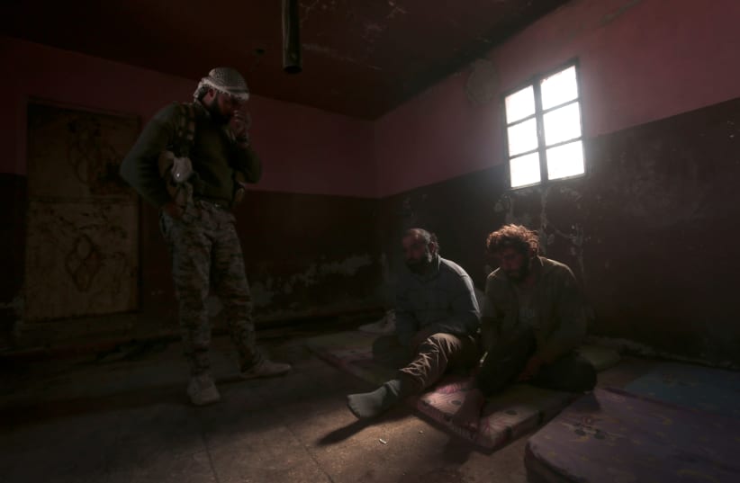 A Syrian Democratic Forces (SDF) fighter stands near who he said were Islamic State fighters held prisoners, north of Raqqa city, Syria March 8, 2017 (photo credit: RODI SAID / REUTERS)